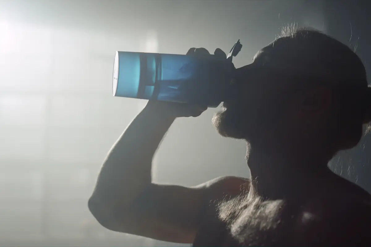 Silhouetted figure drinking from water bottle against bright background, capturing post-workout hydration and recovery moment
