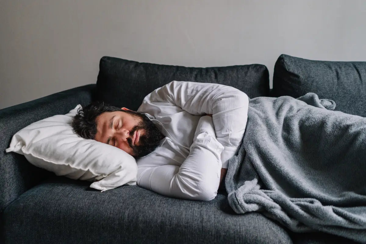 Person sleeping deeply on couch with white pillow and gray blanket, showing quality sleep state