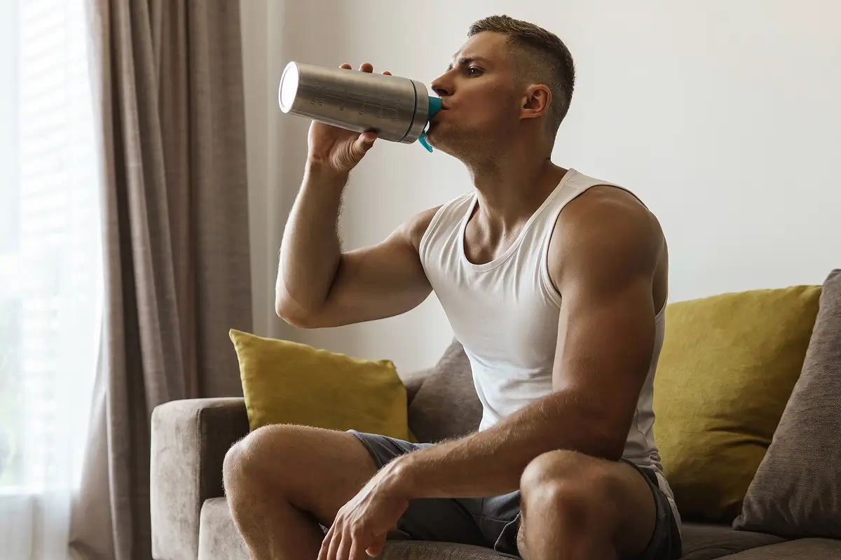 Man drinking from shaker bottle on couch