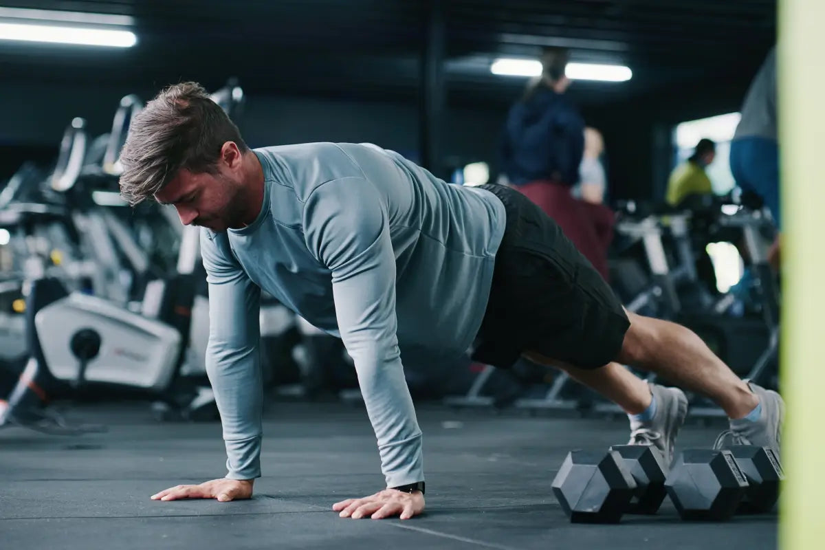 Person performing push-up in gym setting with dumbbells, demonstrating workout intensity and training performance